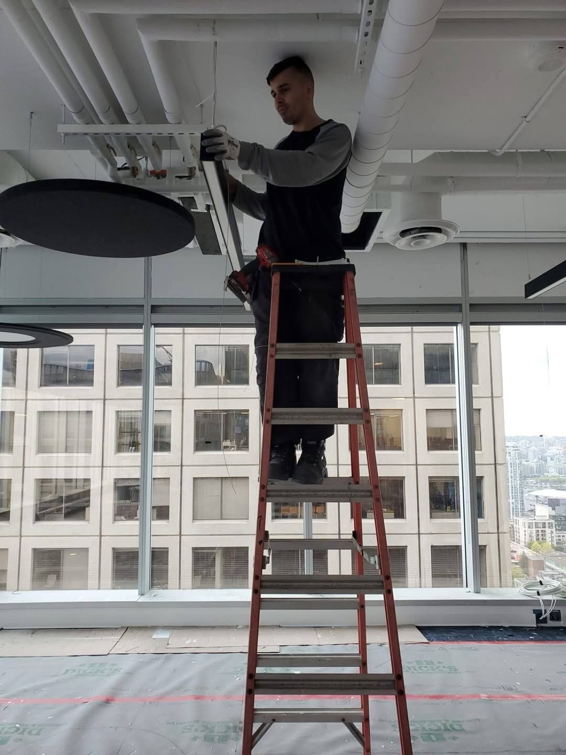 Electrician on ladder installing commercial light fixture